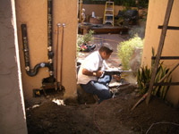 Alfredo an electrical guy drills into the wall, to set up conduit between the shed and the house.  On the left are the outdoor Washer/Dryer hookups.  In the background is a fountain of a boy peeing